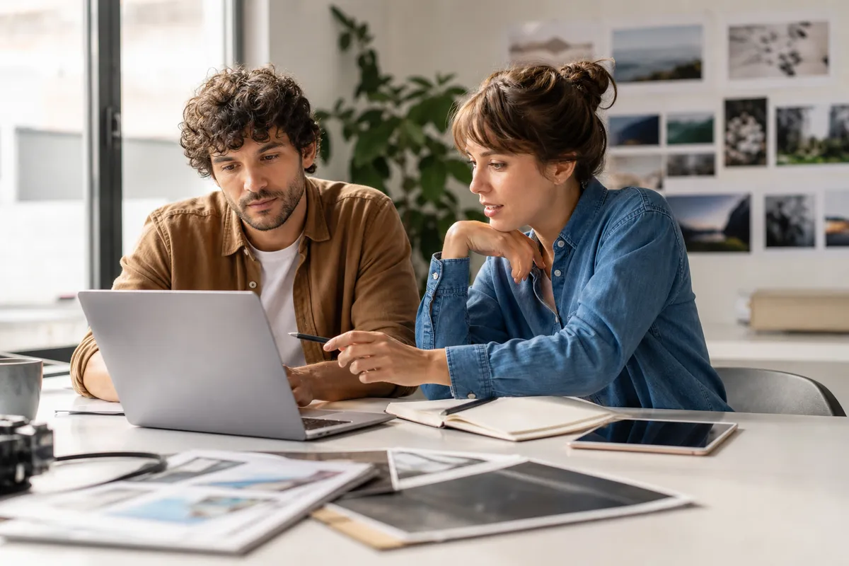 Small creative team reviewing client approval feedback on a laptop in a bright studio