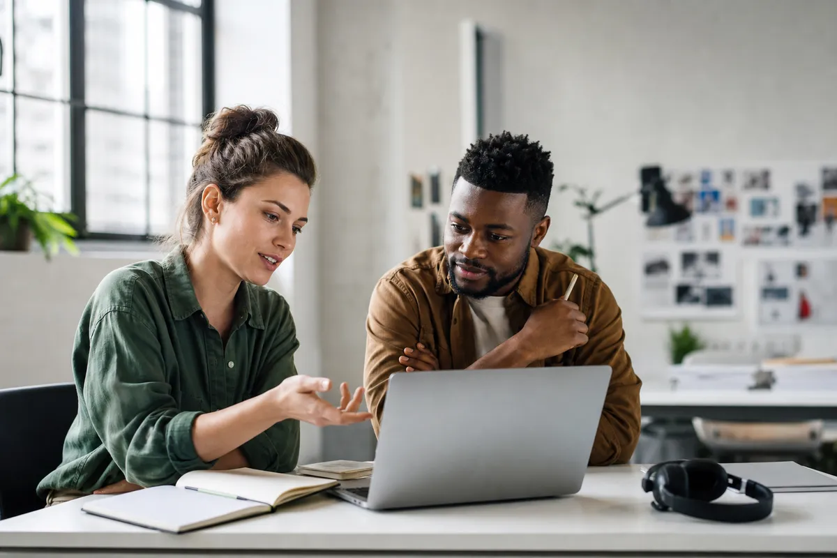 Freelancer and teammate reviewing client feedback together on a laptop in a bright creative studio